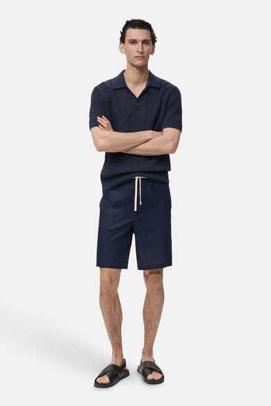 Korte blauwe broek van MANGO, met trekkoord en gedragen met een gebreid poloshirt en leren sandalen.