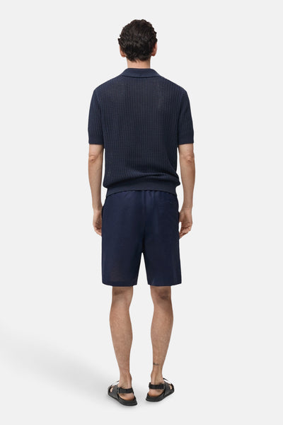 Short bleu de MANGO, porté avec un polo texturé et des sandales en cuir, vue de dos.

