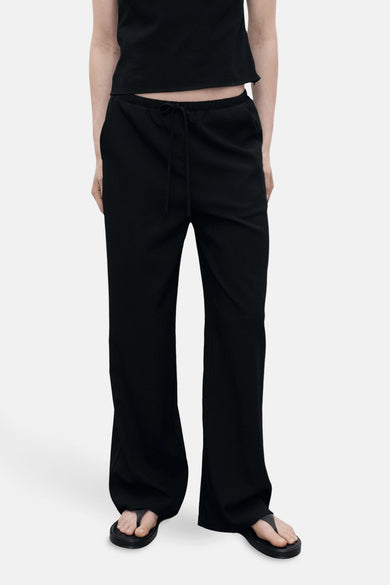 Zwarte broek van MANGO, losse pasvorm met een gladde textuur, van achteren zichtbaar met een bijpassend zwart topje.