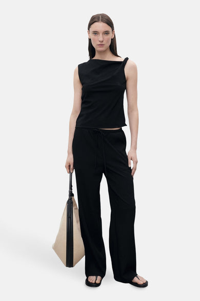 Zwarte broek met wijde pijpen van MANGO, gedragen met een asymmetrische zwarte top en zwarte teenslippers.