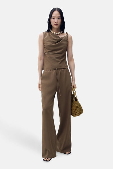 Bruine broek van MANGO, uitlopend model, met trekkoord, gedragen met een top en een parelketting.