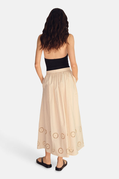 Lange beige rok van MANGO, met decoratieve uitgesneden patronen aan de onderkant en zijzakken, gedragen met een zwarte top.