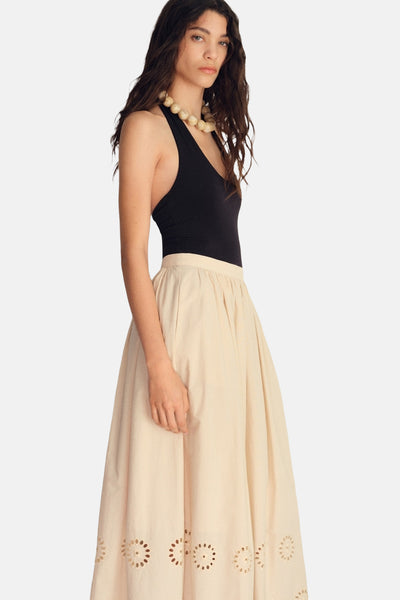 Jupe longue beige de MANGO, avec broderie anglaise florale sur l'ourlet, portée avec un body noir et un collier de perles.