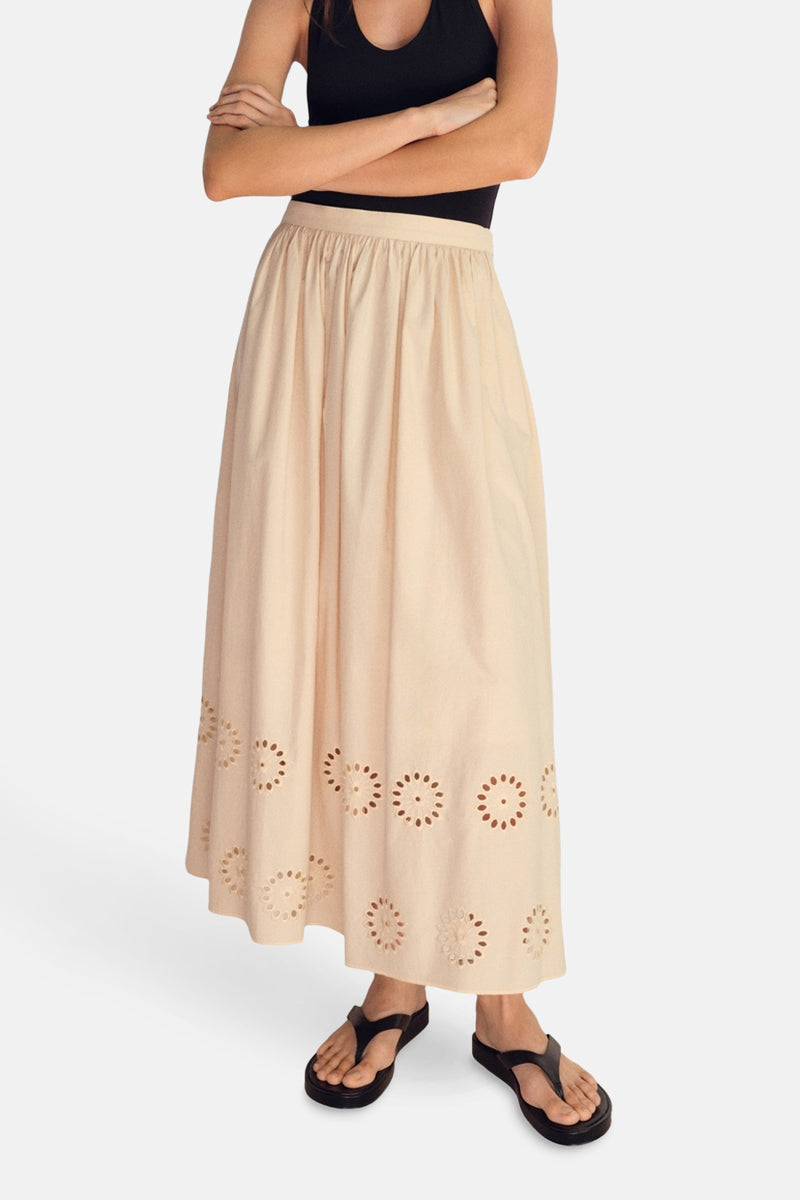 Lange beige rok van MANGO, met bloemenpatronen met uitsparingen, gedragen met een zwarte tanktop en sandalen.