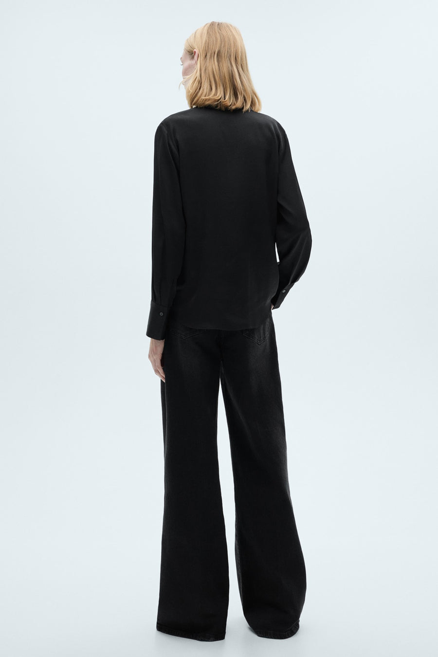Zwart overhemd met lange mouwen van MANGO, van achteren gezien, gedragen met een zwarte high-waist jeans.