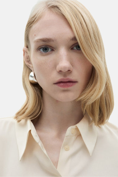 Wit katoen chemisier met lange mouwen van MANGO, gedragen met een knop open op de collar en zilveren oorhangers.