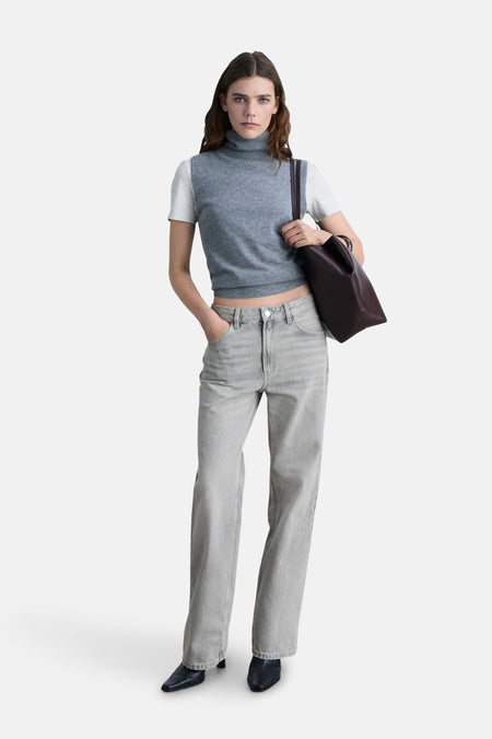 Jean droit gris moyen de MANGO, porté avec un pull sans manches gris et un sac à main marron.