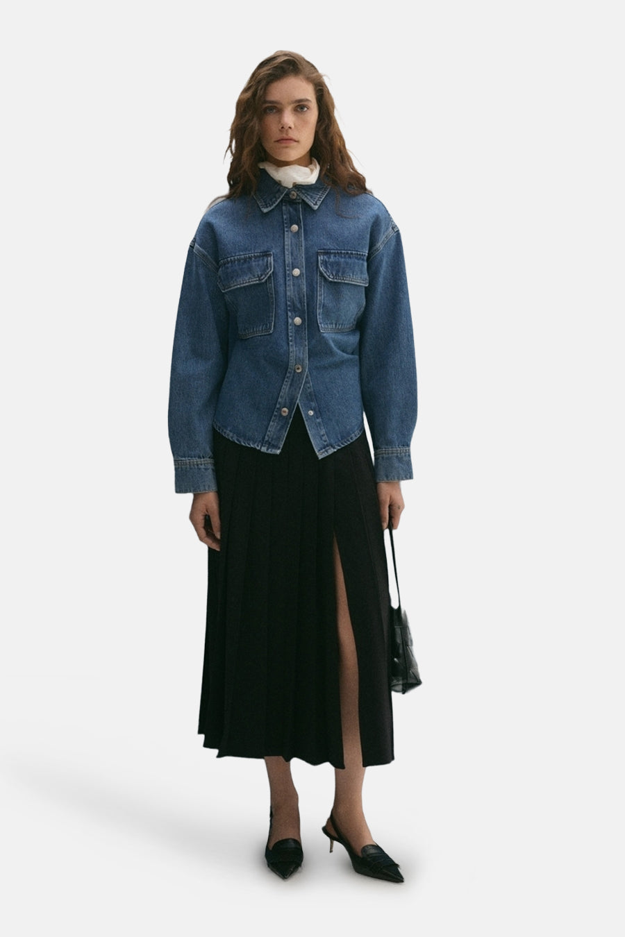 Veste courte en denim bleu moyen de MANGO, portée sur un col roulé blanc et une jupe noire plissée fendue.