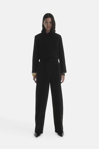 Blazer noir de MANGO, porté avec un pantalon taille haute assorti et des chaussures pointues.
