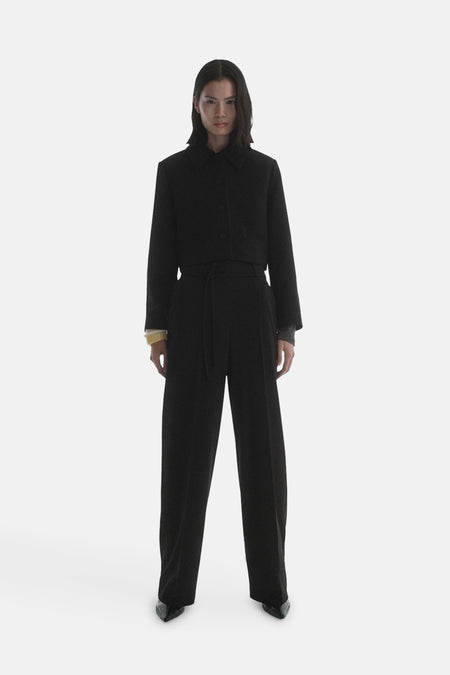 Blazer noir de MANGO, porté avec un pantalon taille haute assorti et des chaussures pointues.