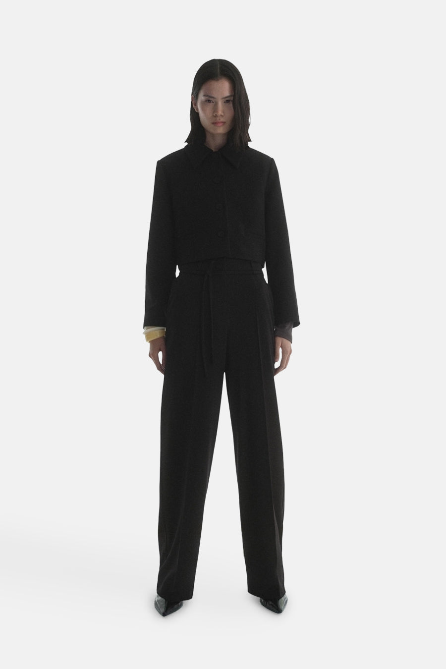 Blazer noir de MANGO, porté avec un pantalon taille haute assorti et des chaussures pointues.