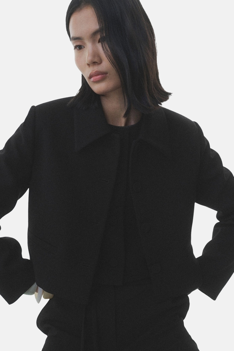 Zwarte blazer van MANGO, gedragen met een zwart T-shirt en een bijpassende broek, handen in de zij.