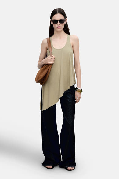 Blouse kaki sans manches de MANGO, coupe asymétrique, portée avec un sac bandoulière marron et un jean.
