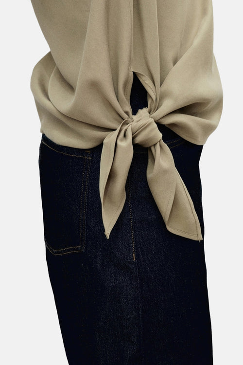 Blouse kaki de MANGO, nouée sur le côté, portée avec un jean bleu foncé.