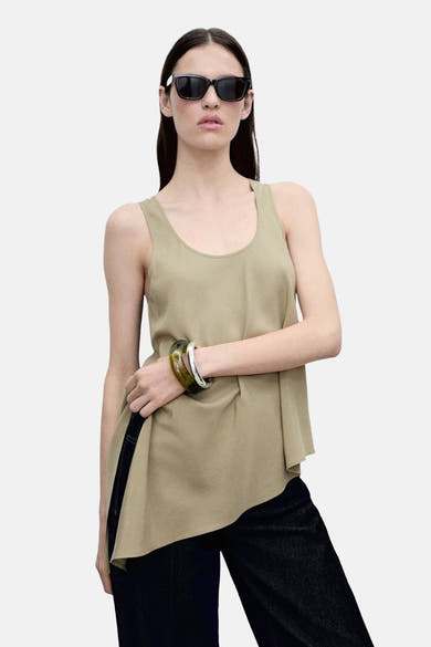 Blouse kaki sans manches de MANGO, avec des bracelets verts et argentés et un pantalon noir.