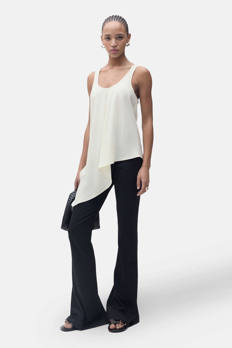 Ecru mouwloos blouse van MANGO, asymmetrisch, gedragen met een zwarte wijde broek en sandalen.