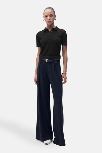 Polo noir à manches courtes de MANGO, porté avec un pantalon large à taille haute et une ceinture fine.
