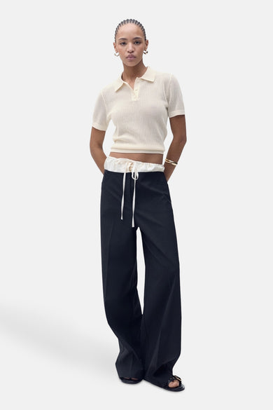 Polo beige à manches courtes de MANGO, en maille côtelée, porté avec un pantalon taille haute à cordon.
