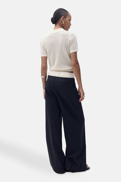 Polo beige à manches courtes de MANGO, en maille côtelée, porté avec un pantalon taille haute noir.