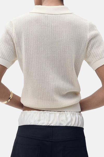 Polo beige à manches courtes de MANGO, tricoté avec une texture ajourée et porté avec un pantalon noir.
