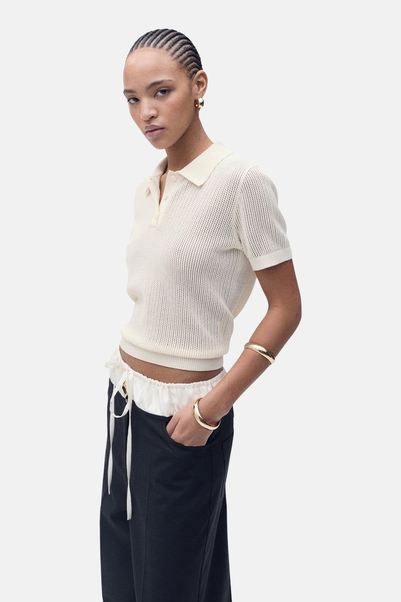 Polo beige à manches courtes de MANGO, en maille ajourée, porté avec un pantalon taille haute.
