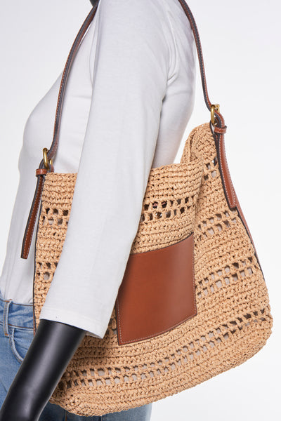 Sac à bandoulière en paille marron de MANGO avec une poche en cuir marron, porté avec un t-shirt blanc.
