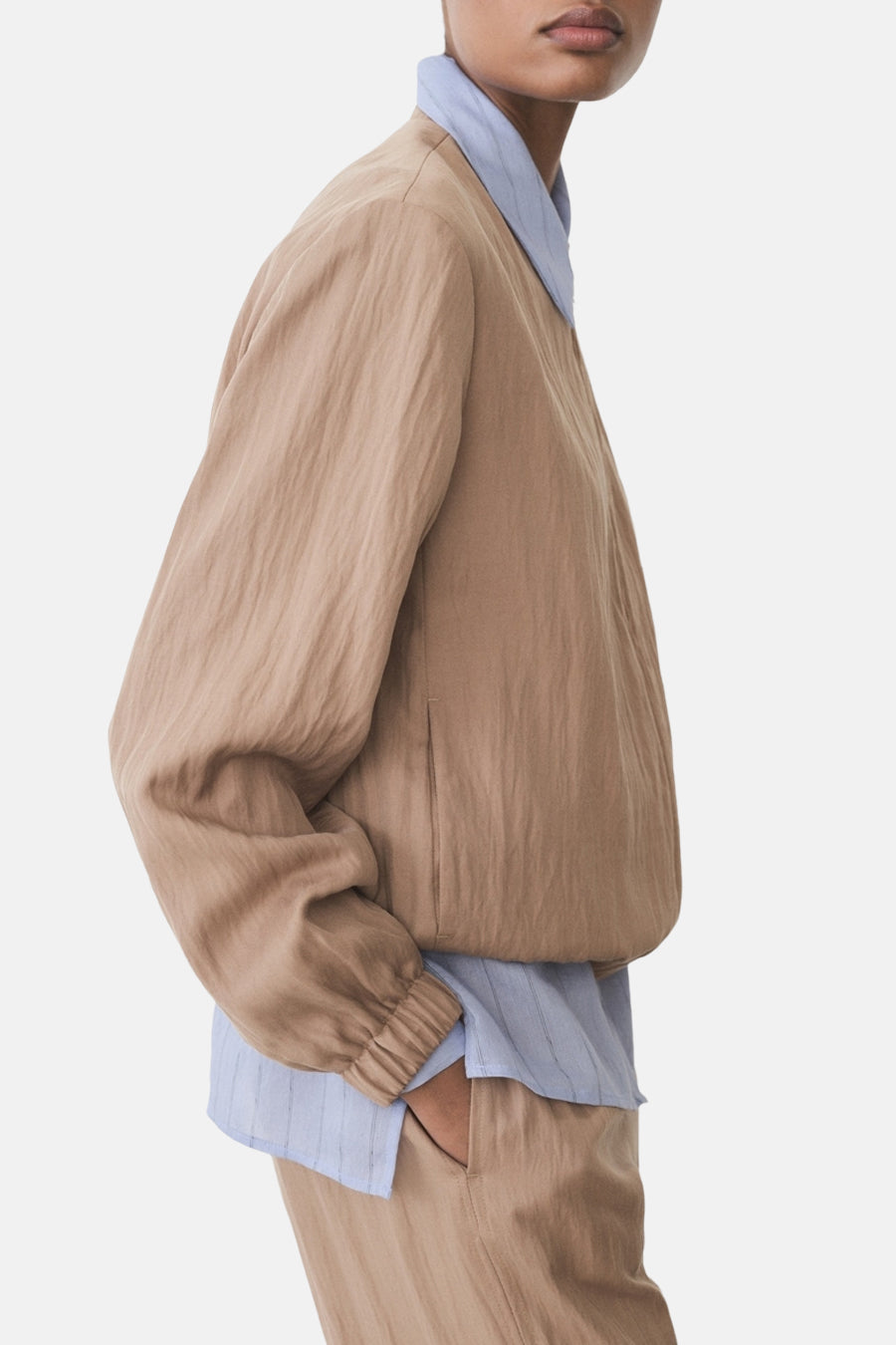 Veste courte brune de MANGO avec une texture froissée, portée sur une chemise bleue à rayures.