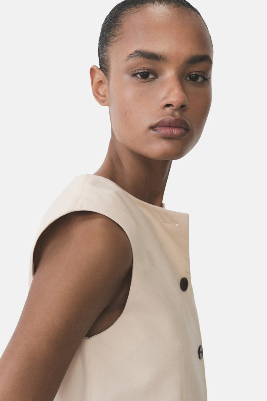Blazer écru de MANGO, coupe sans manches avec boutons foncés, porté par un mannequin à la peau hâlée.