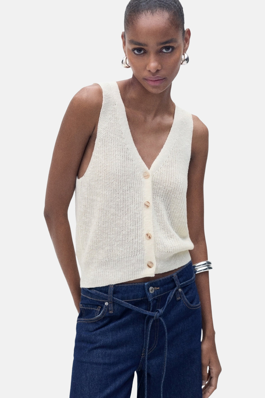 Débardeur écru en maille de MANGO, avec boutonnage sur le devant, porté avec un jean taille haute.
