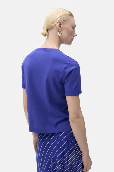 Pull à col rond bleu de MANGO, vu de dos, porté avec une jupe rayée.