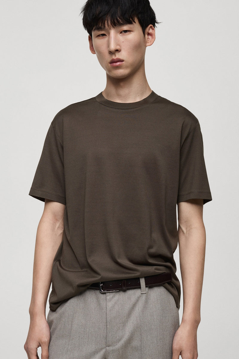 Kaki T-shirt met korte mouwen van MANGO, gedragen met een lichtgrijze broek, achtergezicht.