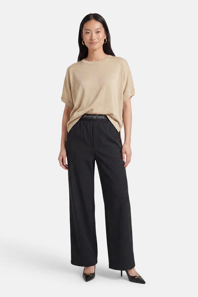 Golden short-sleeve T-shirt by Alexander Wang, featuring a relaxed fit and ribbed texture, worn with black wide-leg pants and pointed heels.