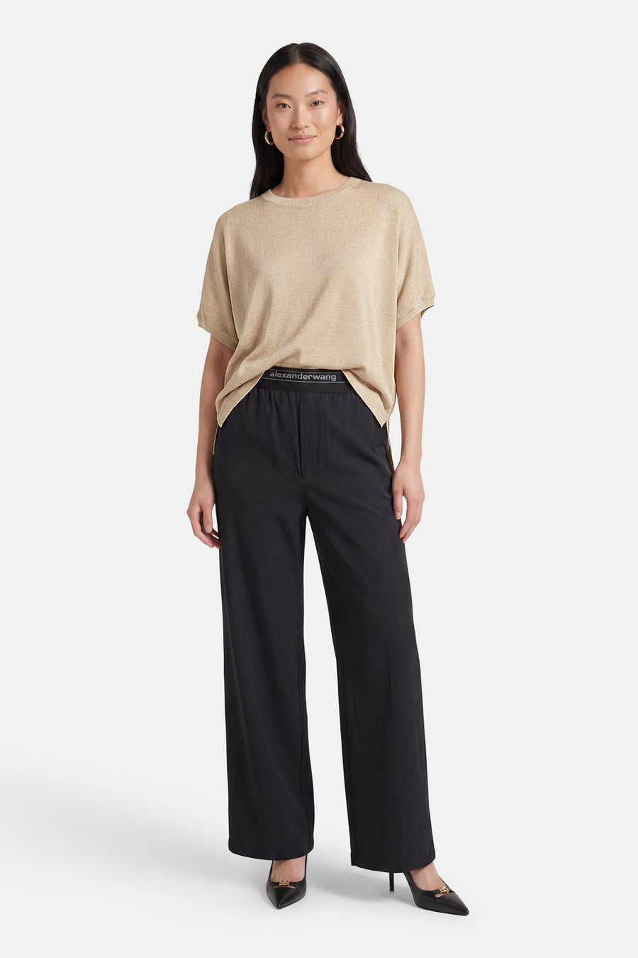 Golden short-sleeve T-shirt by Alexander Wang, featuring a relaxed fit and ribbed texture, worn with black wide-leg pants and pointed heels.
