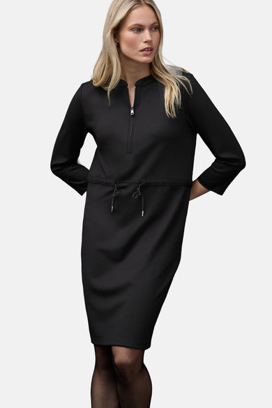 Robe noire de STREET ONE avec fermeture éclair et cordon de serrage, portée avec des collants noirs.