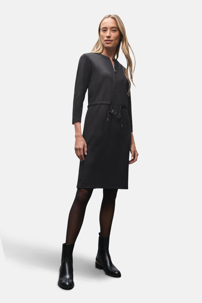 Zwarte jurk van STREET ONE met ritssluiting en trekkoord in de taille, gedragen met panty en enkellaarsjes.