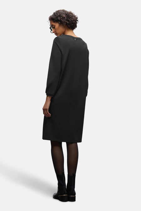 Robe noire de Street One, manches longues, portée avec des collants et des bottines noires.