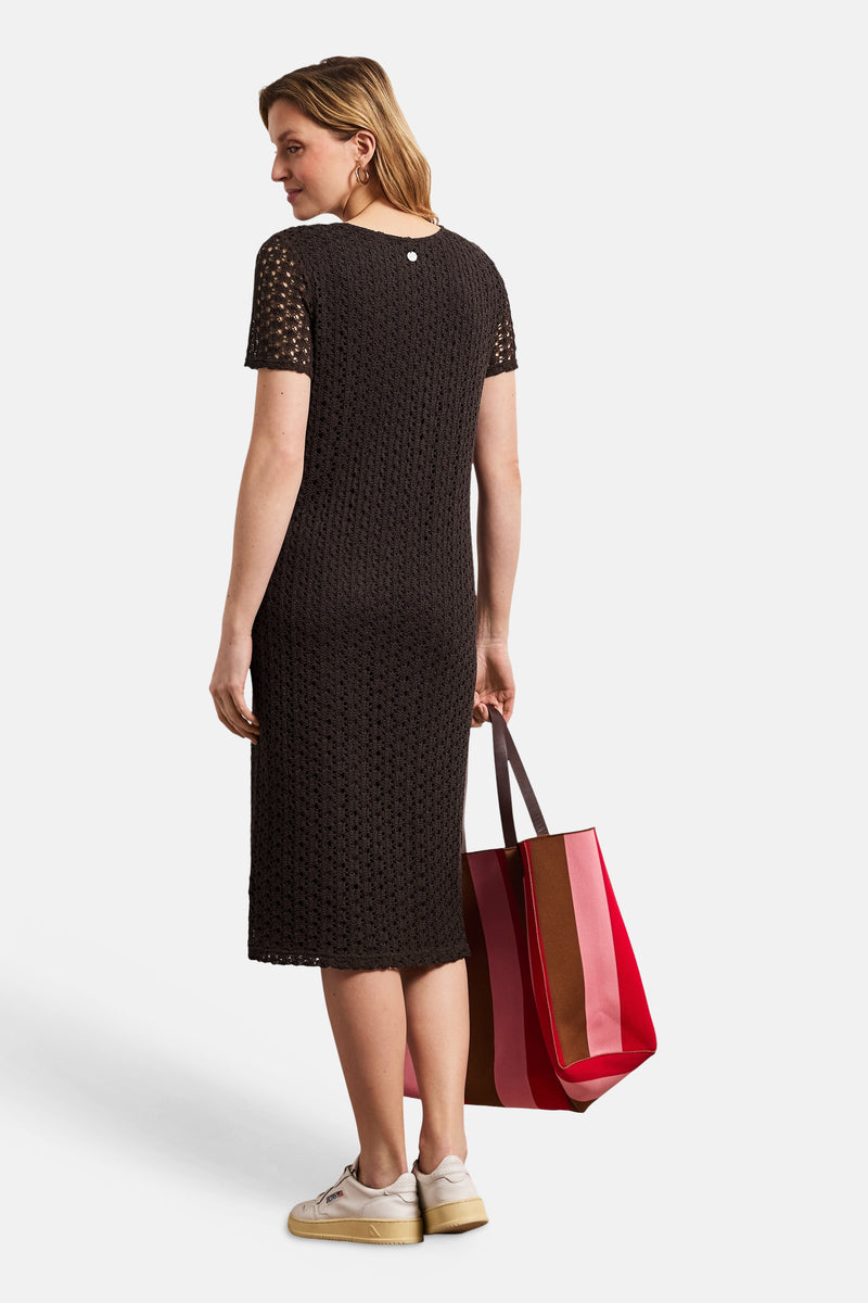 Robe midi brune de STREET ONE en maille ajourée, manches courtes et bouton argenté au dos, vue de dos. Le modèle tient un sac rayé et porte des baskets.