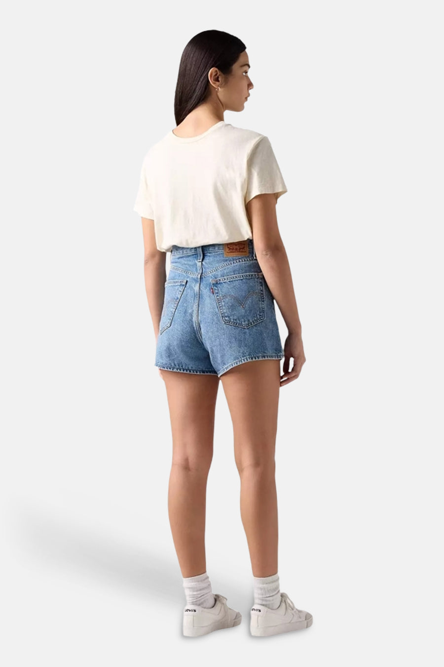 Short en denim par Levi's, avec une taille haute et une coupe décontractée, porté avec un t-shirt blanc cassé et des baskets.
