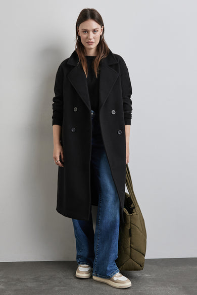 Manteau long noir de STREET ONE, porté avec un pull noir, un jean bleu et des baskets beiges.
