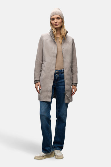 Lange bruine jas van Street One, gedragen met een beige muts, een beige T-shirt en een blauwe spijkerbroek.