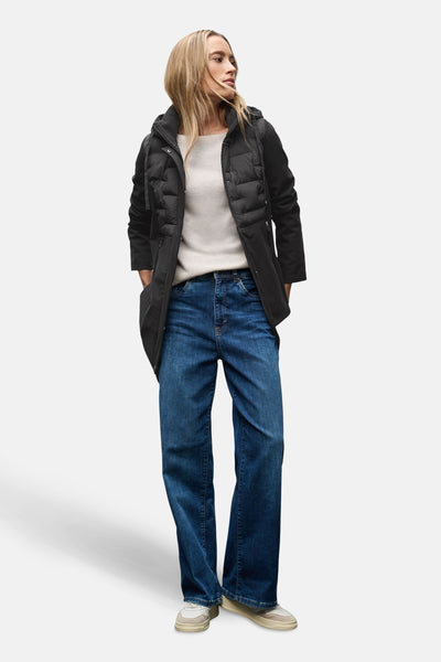 Veste longue noire de Street One, portée avec un pull beige, un jean bleu large et des baskets blanches.
