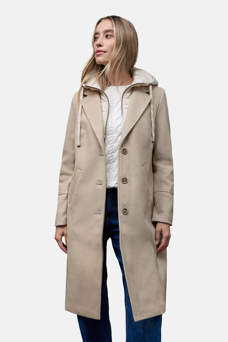 Veste longue beige de Street One avec capuche et fermeture boutonnée, portée sur un pull blanc et un jean.
