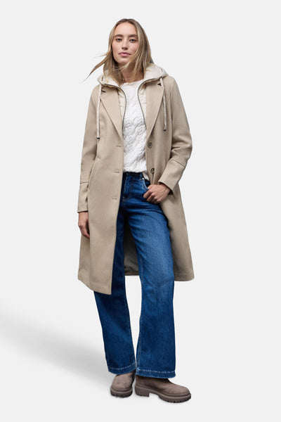 Veste longue beige de Street One avec capuche et fermeture à boutons, portée avec un pull blanc et un jean bleu.