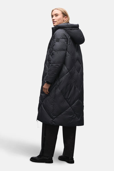 Veste longue bleue de Street One avec motif matelassé en losanges et capuche, portée avec un pantalon foncé et des bottes noires.