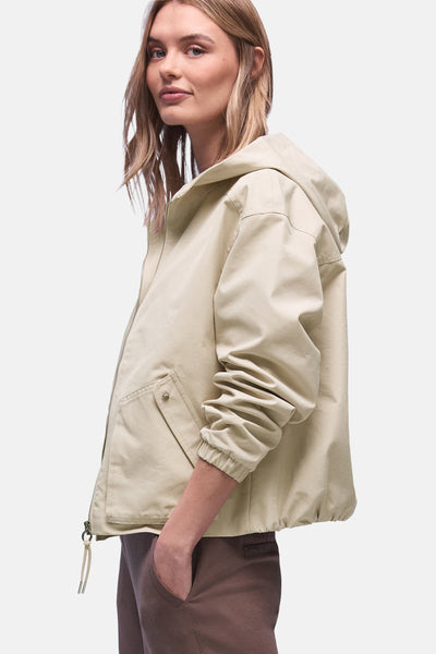 Korte beige jas van STREET ONE met capuchon en elastische lange mouwen, gedragen met een bruine broek.