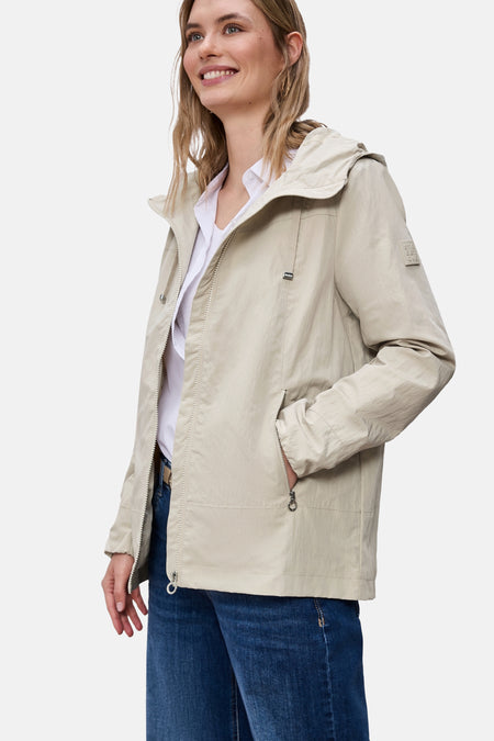 Veste courte beige de Street One avec une capuche et des poches zippées, portée sur une chemise blanche et un jean bleu.