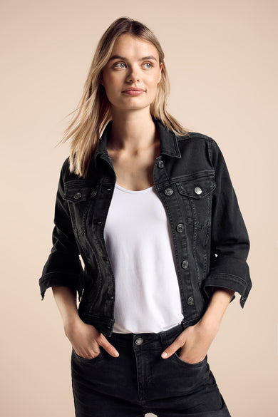 Veste en jean noire de Street One, portée avec un t-shirt blanc et un pantalon noir délavé, mains dans les poches.
