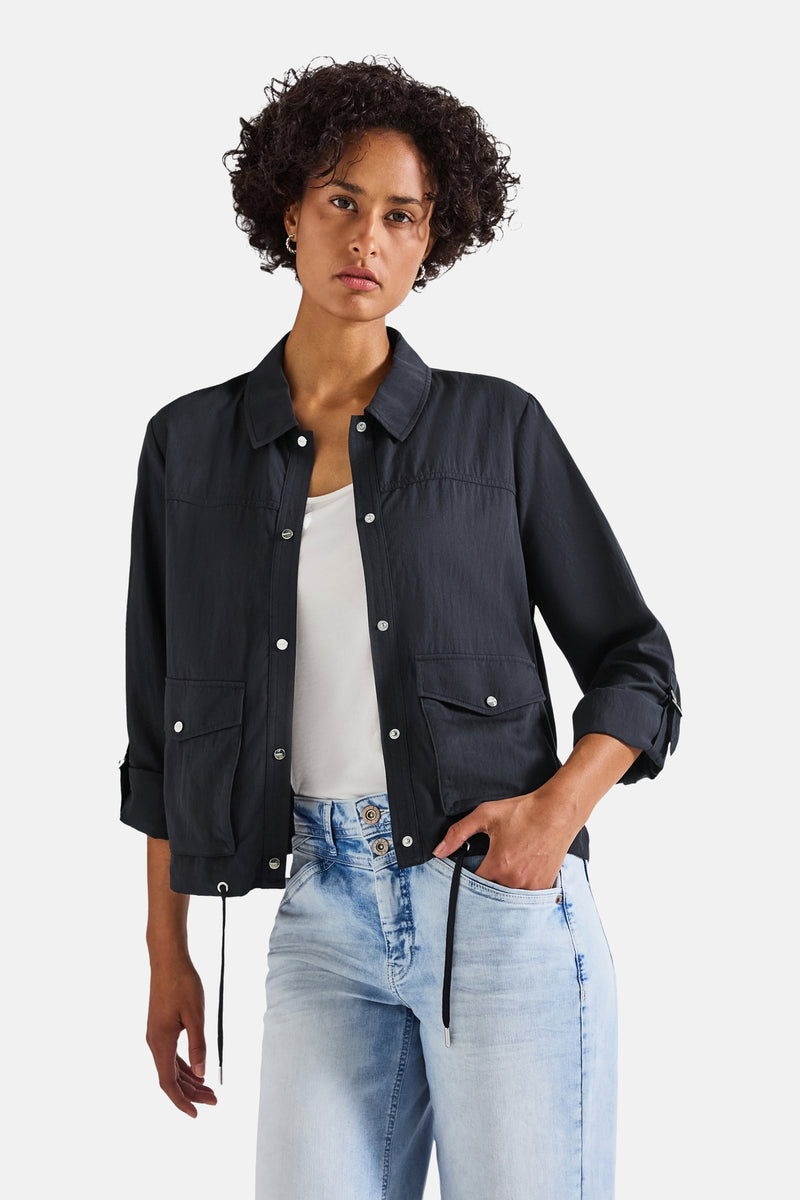 Kort blauw jasje van STREET ONE, met klepzakken en driekwartmouwen die opgerold kunnen worden, gedragen over een witte tanktop en een high-waisted jeans.
