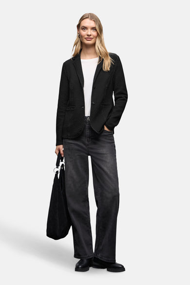 Blazer noir de Street One, à motif texturé, porté avec un t-shirt blanc, un jean foncé et un sac noir.