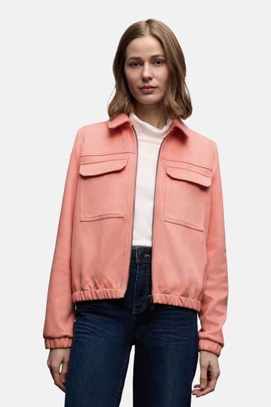 Veste courte corail de Street One, avec poches plaquées et fermeture éclair, portée sur un col roulé blanc et un jean bleu.